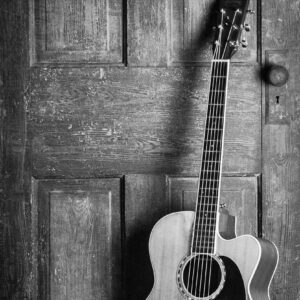 A classic acoustic guitar leaning against a rustic wooden door in a black and white vintage style.